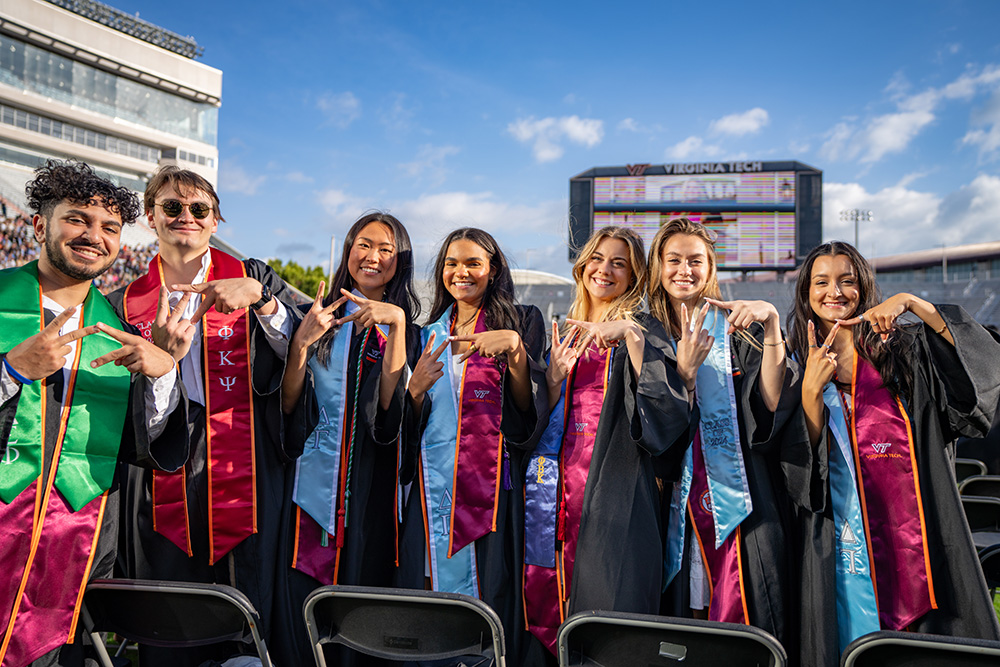 Six graduates make the VT sign with their fingers