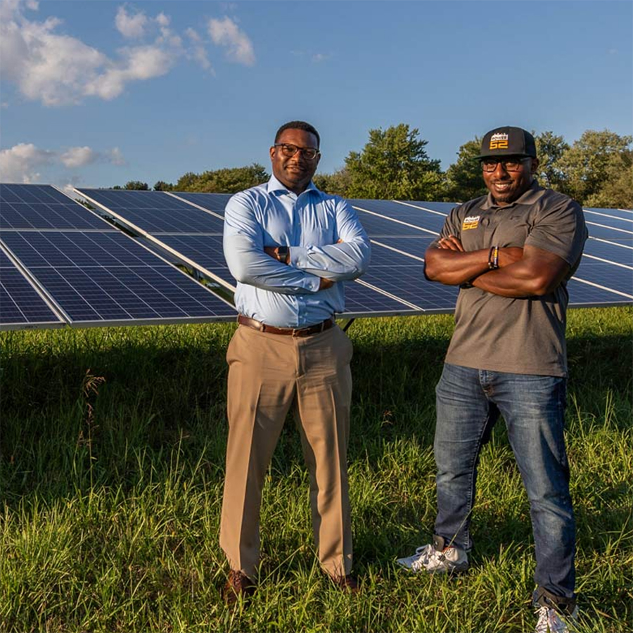 Two alumni stand in a field of solar panels