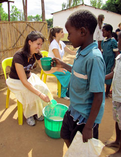 Student Lauren Scheid hands a cup of nsima to a child during a feeding program at Malemia Primary School.