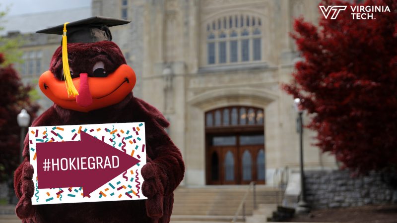 The Hokie Bird holds up a Hokie Grad congratulations sign.